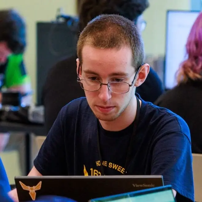 A photo of kieran with a dark navy shirt with an ip address and yellow cyber stinger looking at a laptop screen